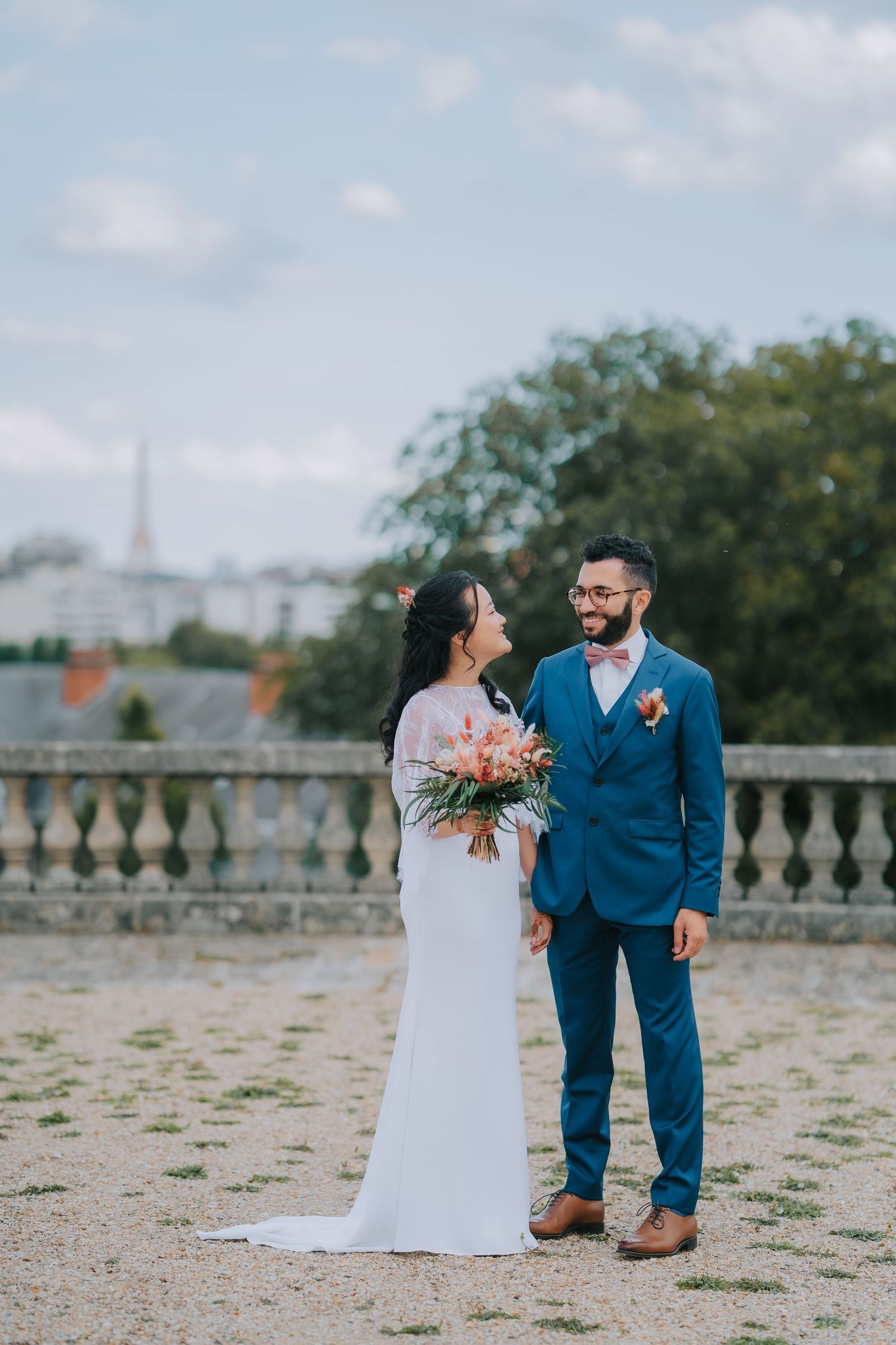 Newlywed couple share a romantic moment at a scenic overlook with the Eiffel Tower visible in the distance.