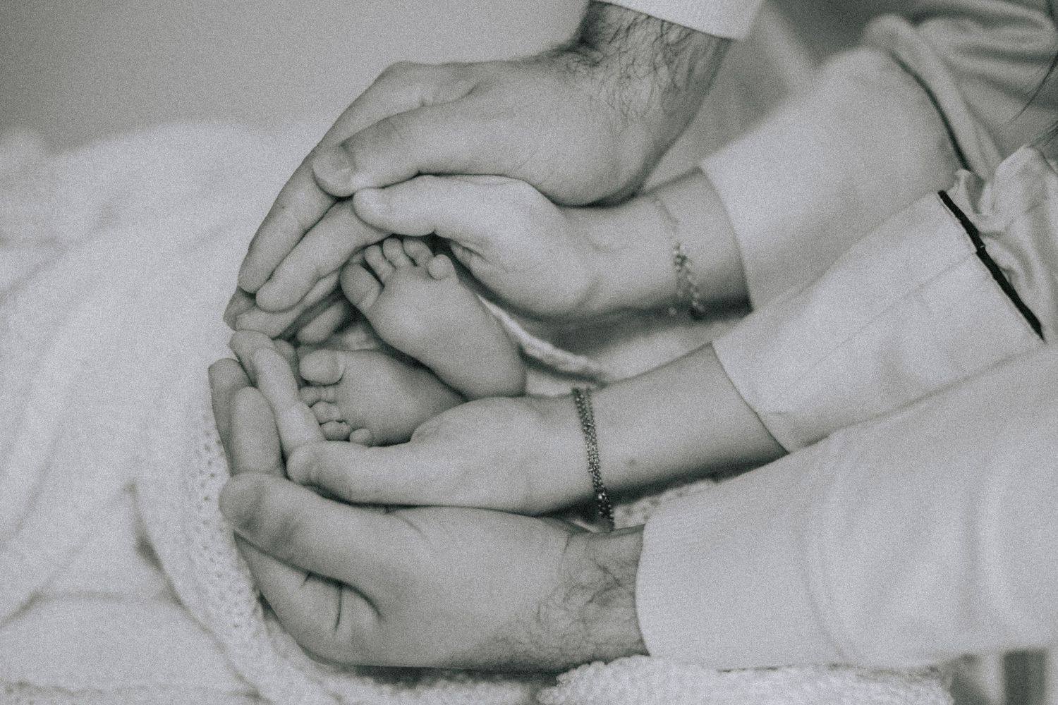 Black and white image of gentle hands cradling small baby feet.