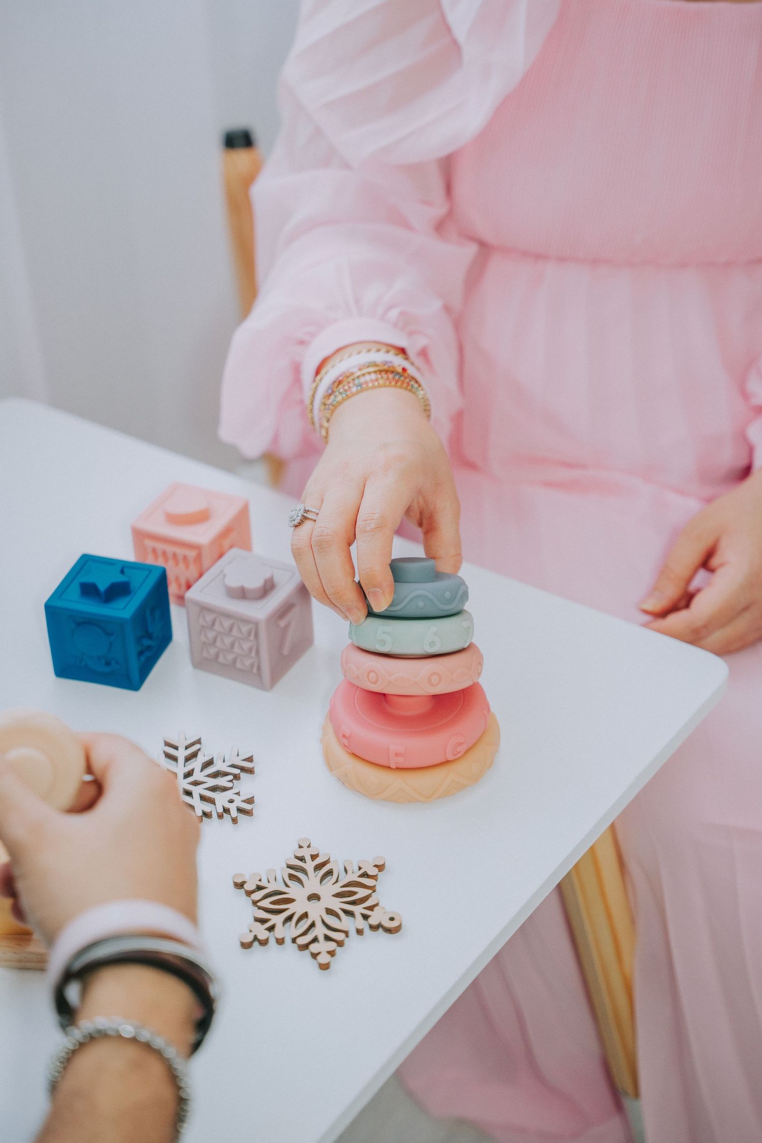 Hands stacking wooden toys on white table with pink dress visible.
