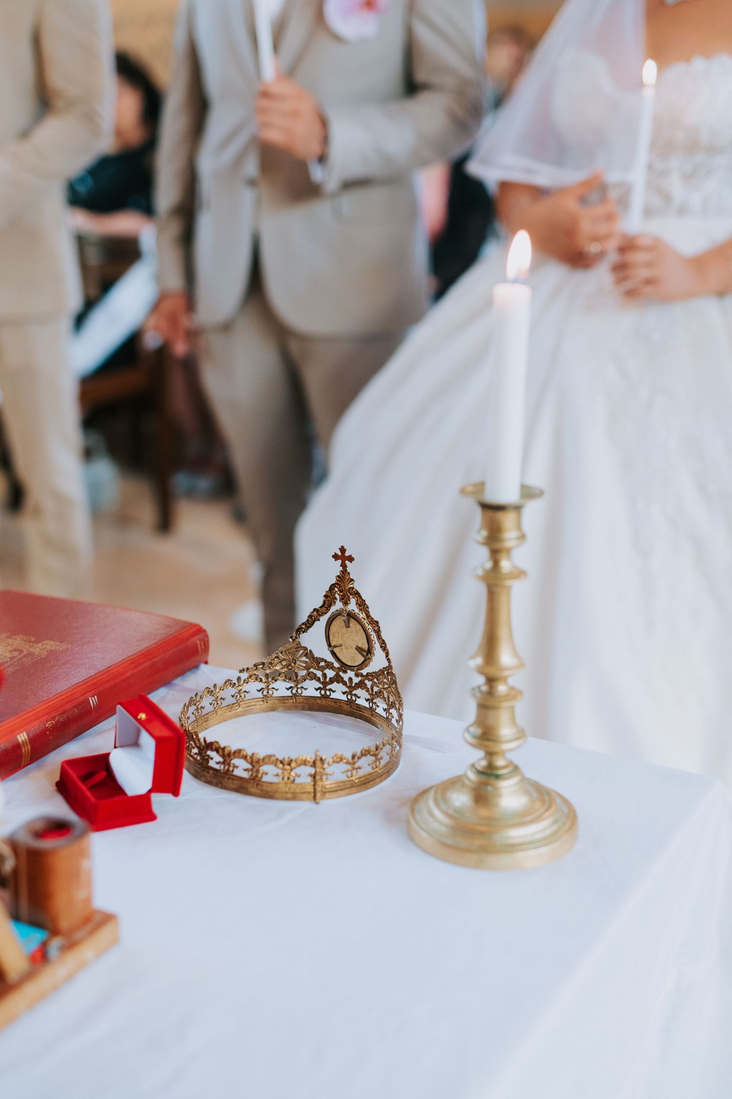Gold ornate crown and brass candlestick on white table during wedding ceremony with couple in background.