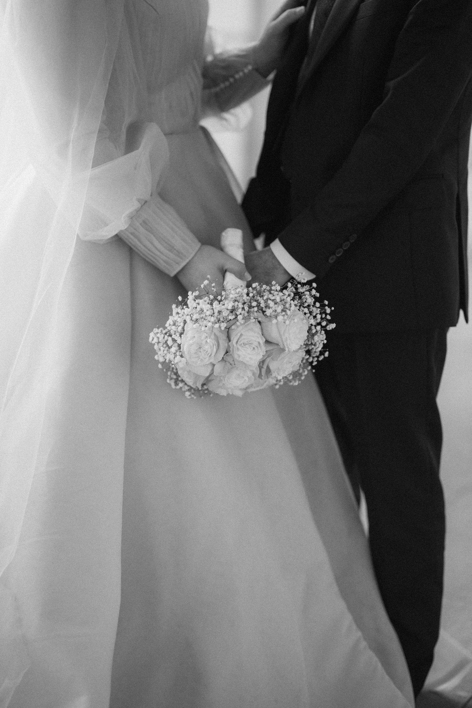 A black and white wedding photo featuring a delicate bouquet of baby's breath flowers between the bride and groom.