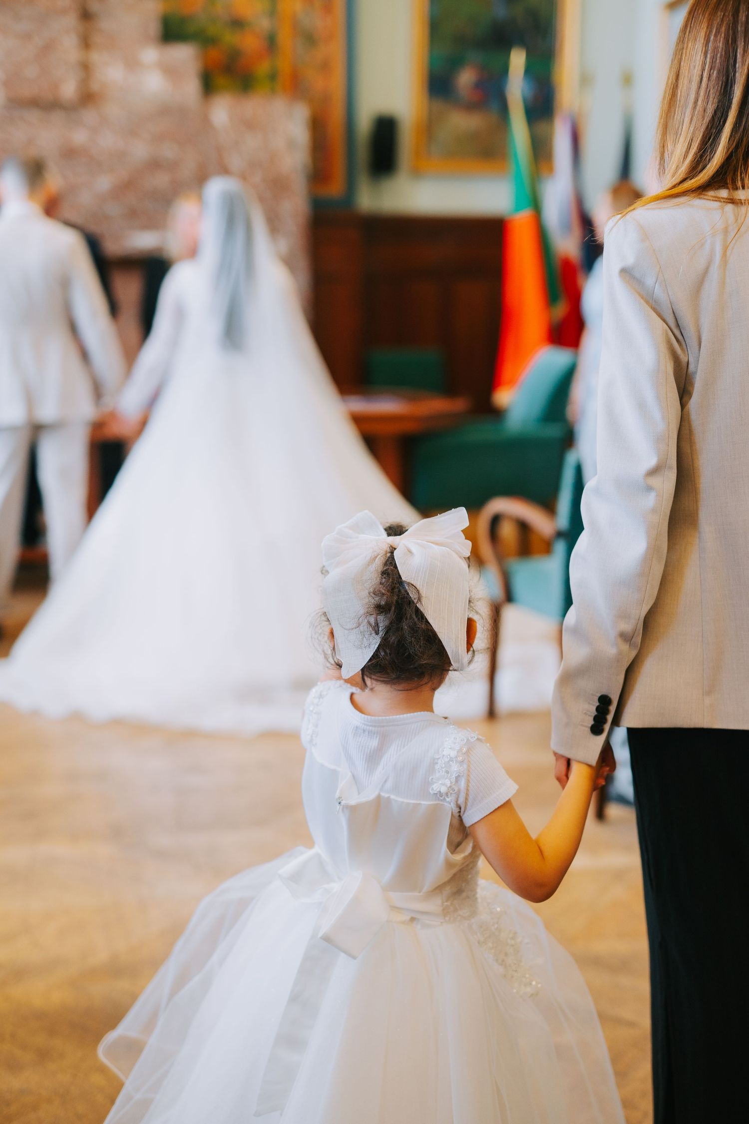 A young girl in a white puffy flower girl dress holds hands with an adult at a wedding ceremony.