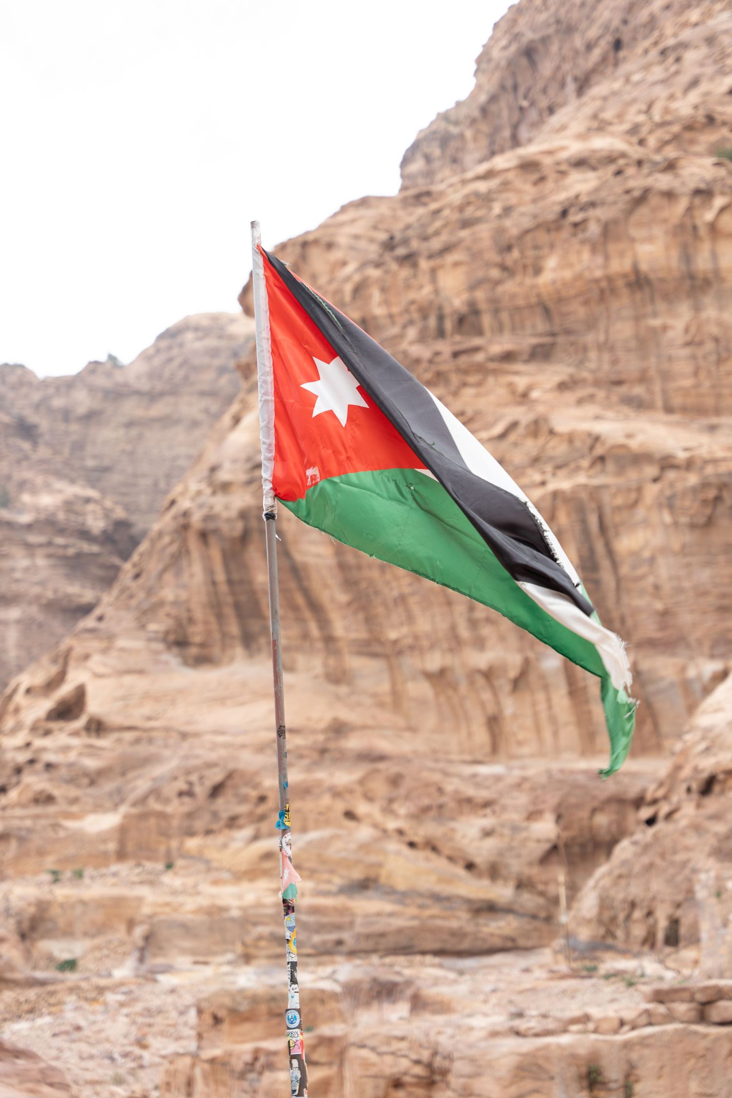 Jordanian flag waving against rocky desert cliffs in Petra.