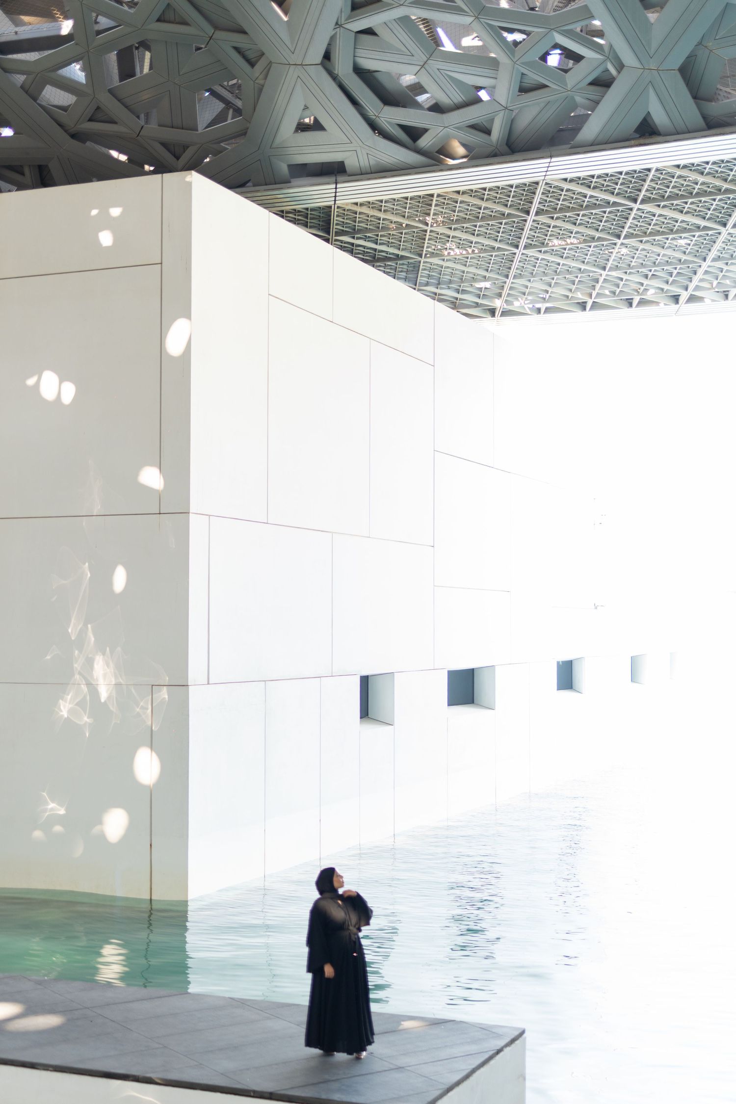 Person in black attire standing by modern white architectural structure with geometric ceiling.