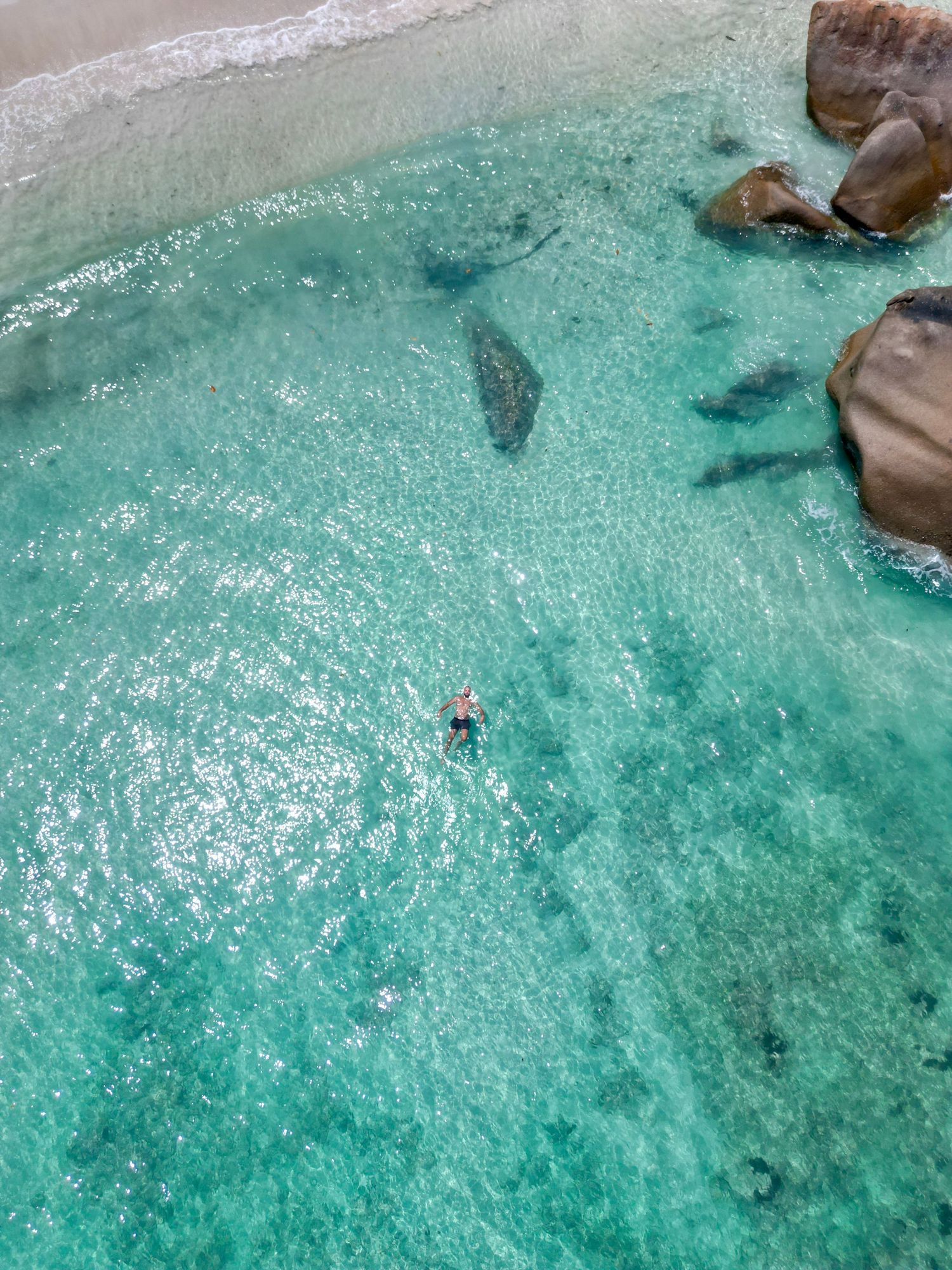 Aerial view of crystal clear turquoise waters with rocks and a swimmer in tropical ocean.