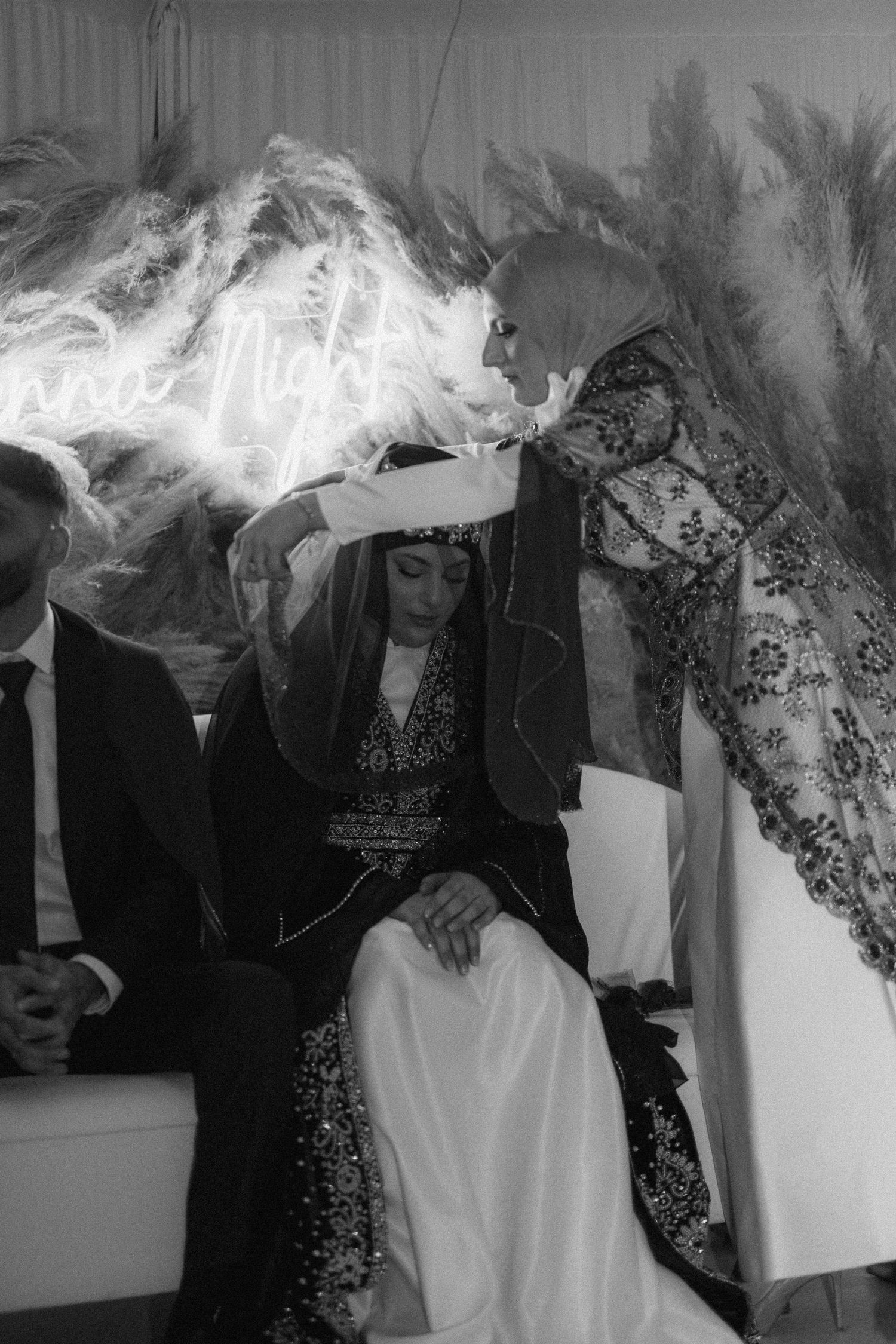 Black and white photo of wedding celebration with neon sign and pampas grass decor.