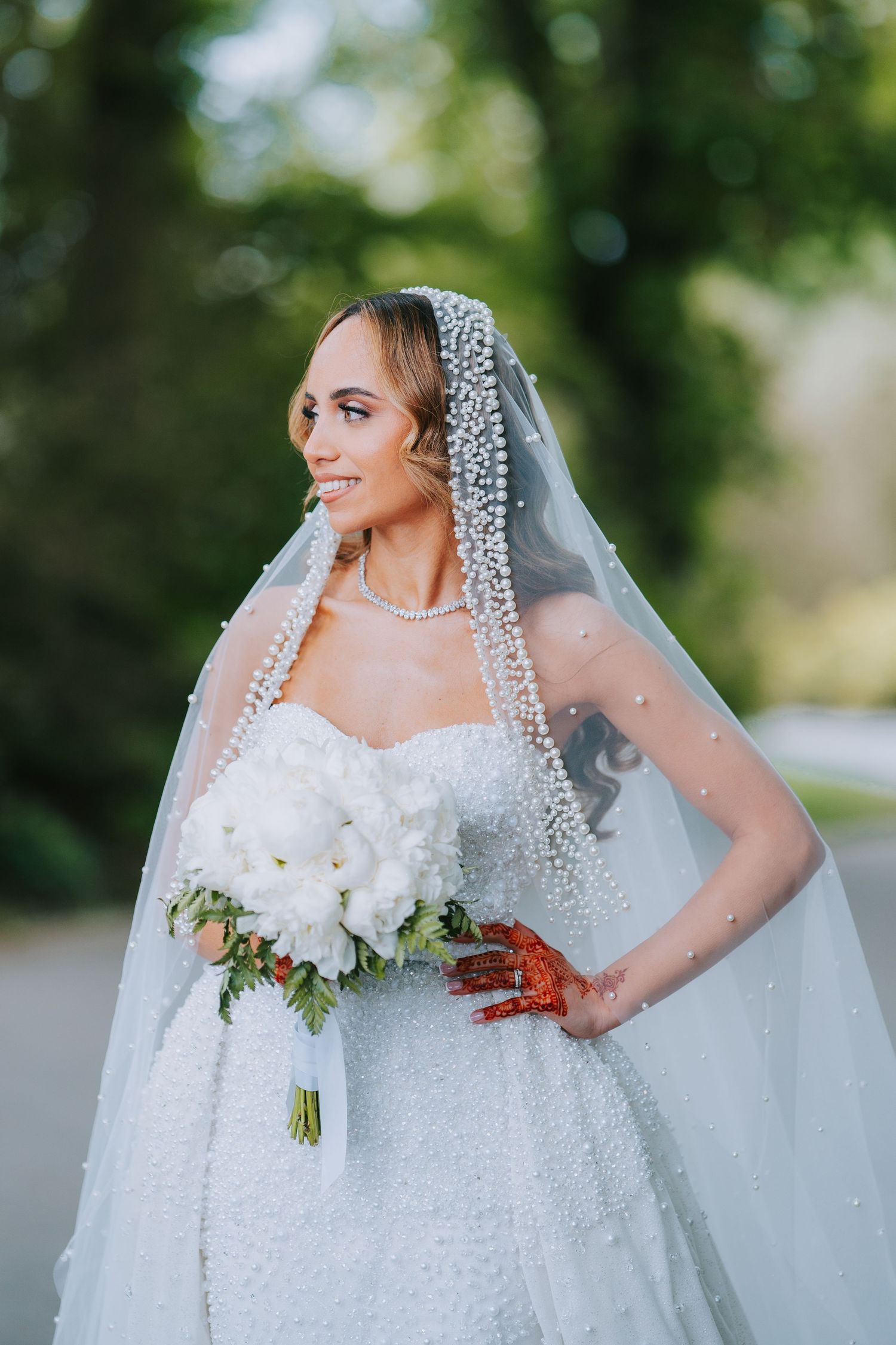 A bride in a sparkly white dress and crystal-embellished veil poses with a bouquet of white flowers.