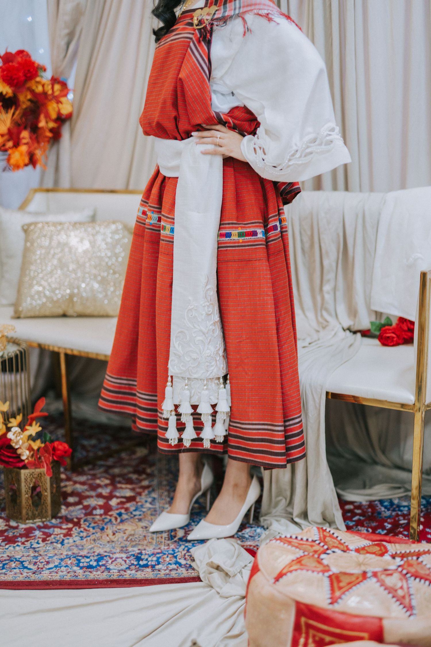 Traditional Ethiopian bridal attire featuring a red embroidered dress with white details and silver heels on ornate carpet.