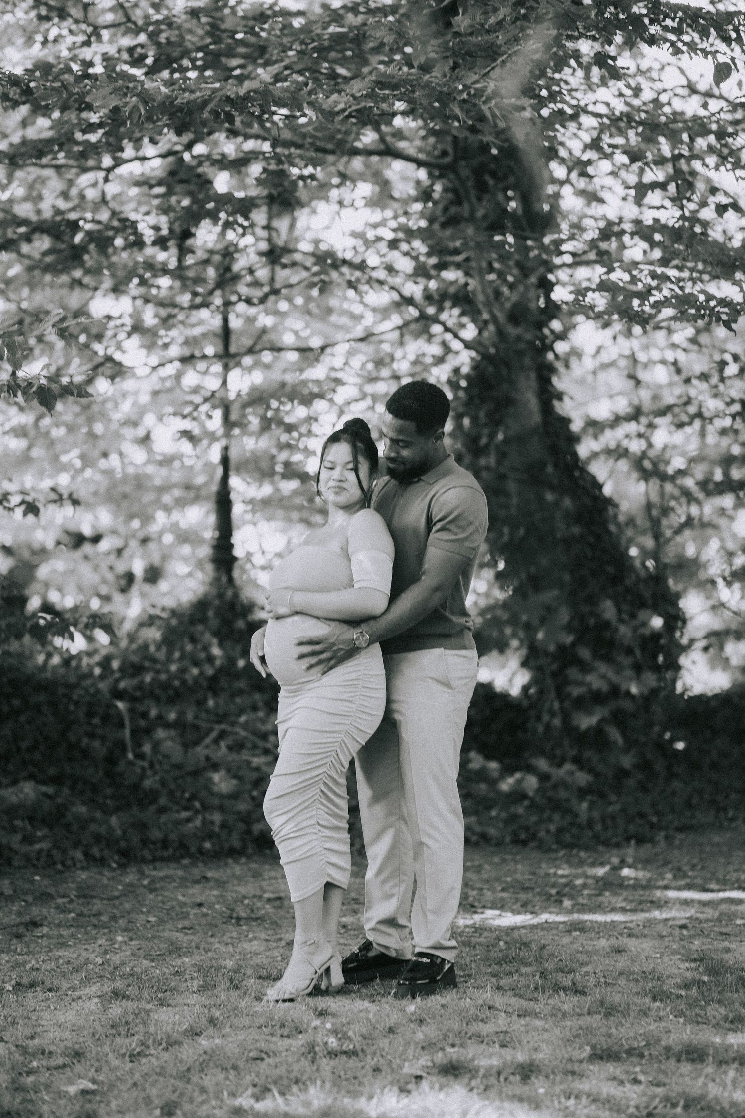 A couple shares an intimate embrace in a black and white forest setting, surrounded by soft natural light and trees.