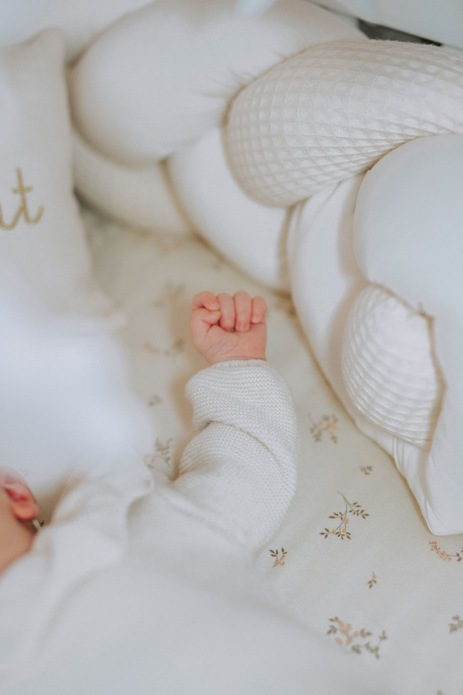 Tiny baby feet in white clothing on delicate patterned fabric.
