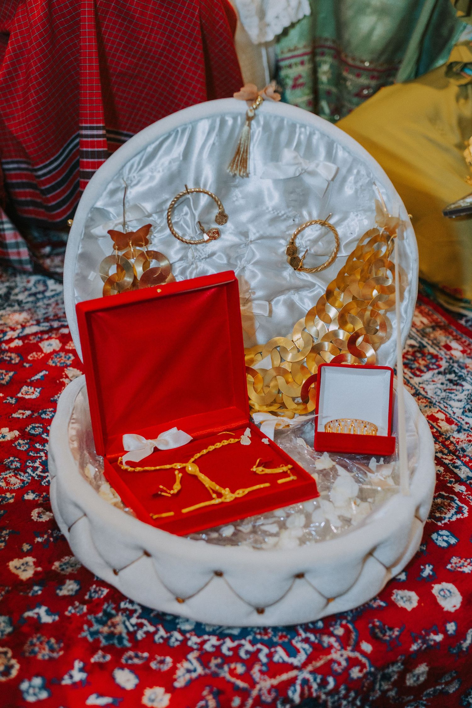 Decorative gold jewelry display on white plate with red velvet box.