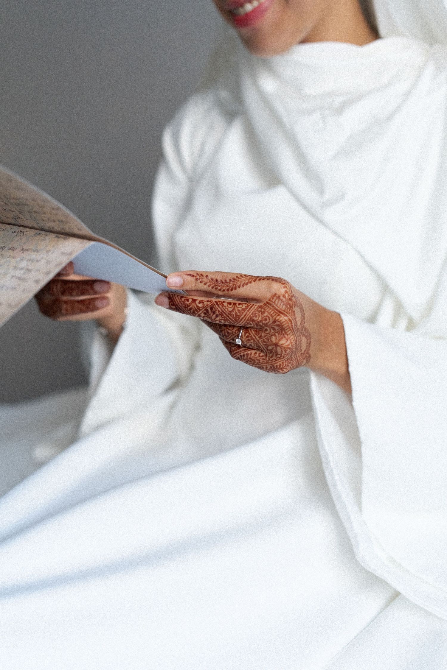 Close-up view of hands with intricate henna designs holding white fabric against a light background.