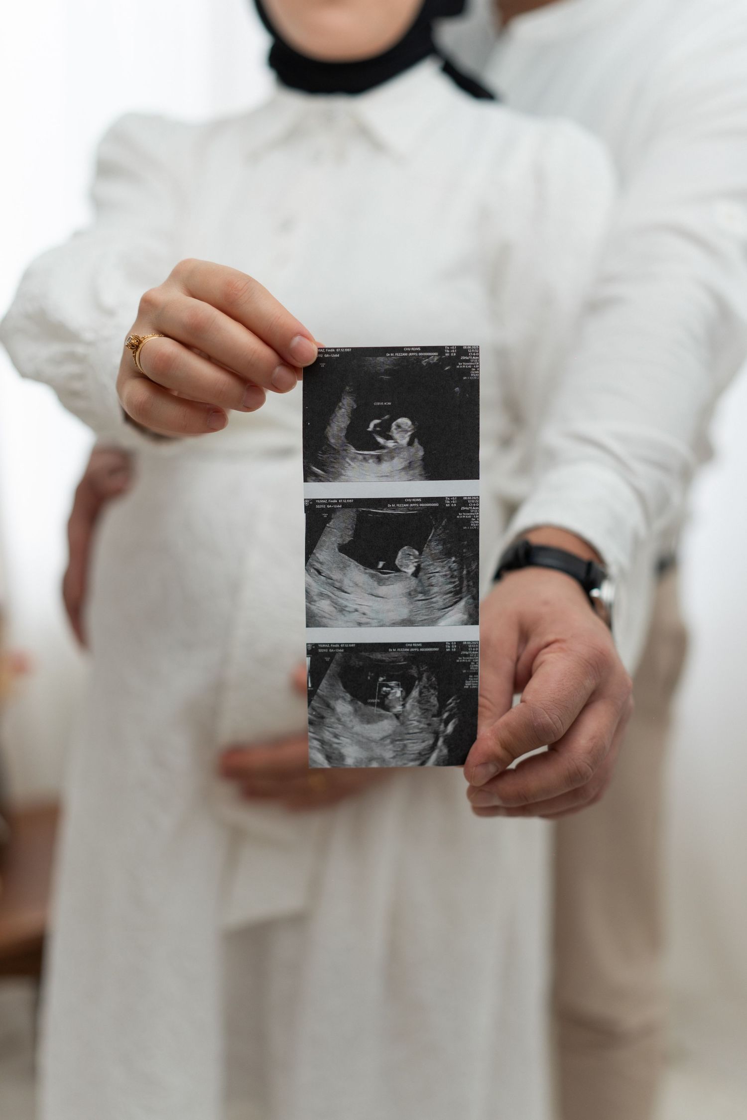 A person in a white outfit holds up ultrasound sonogram photos in a sequence of images.