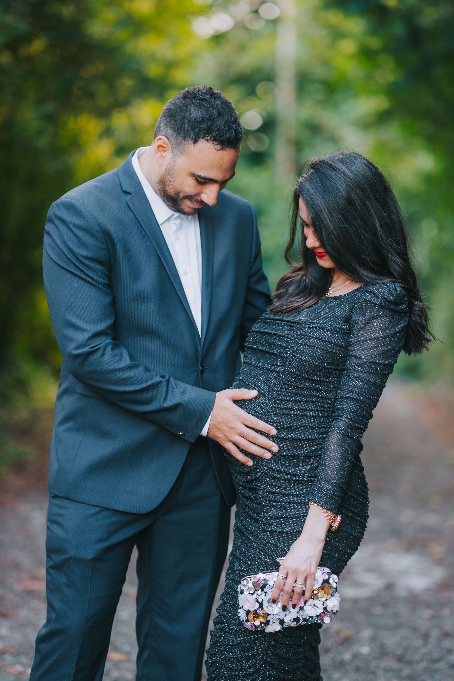 A couple in formal attire share an intimate moment outdoors, with the woman wearing a sparkly black dress.