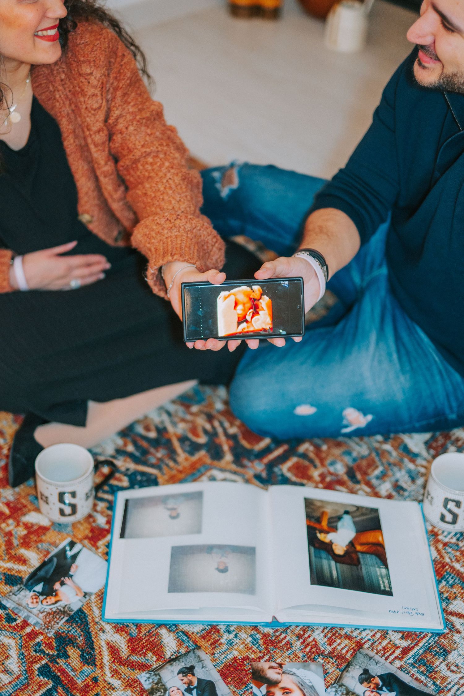 People looking at photos on a phone while sitting on a patterned rug.