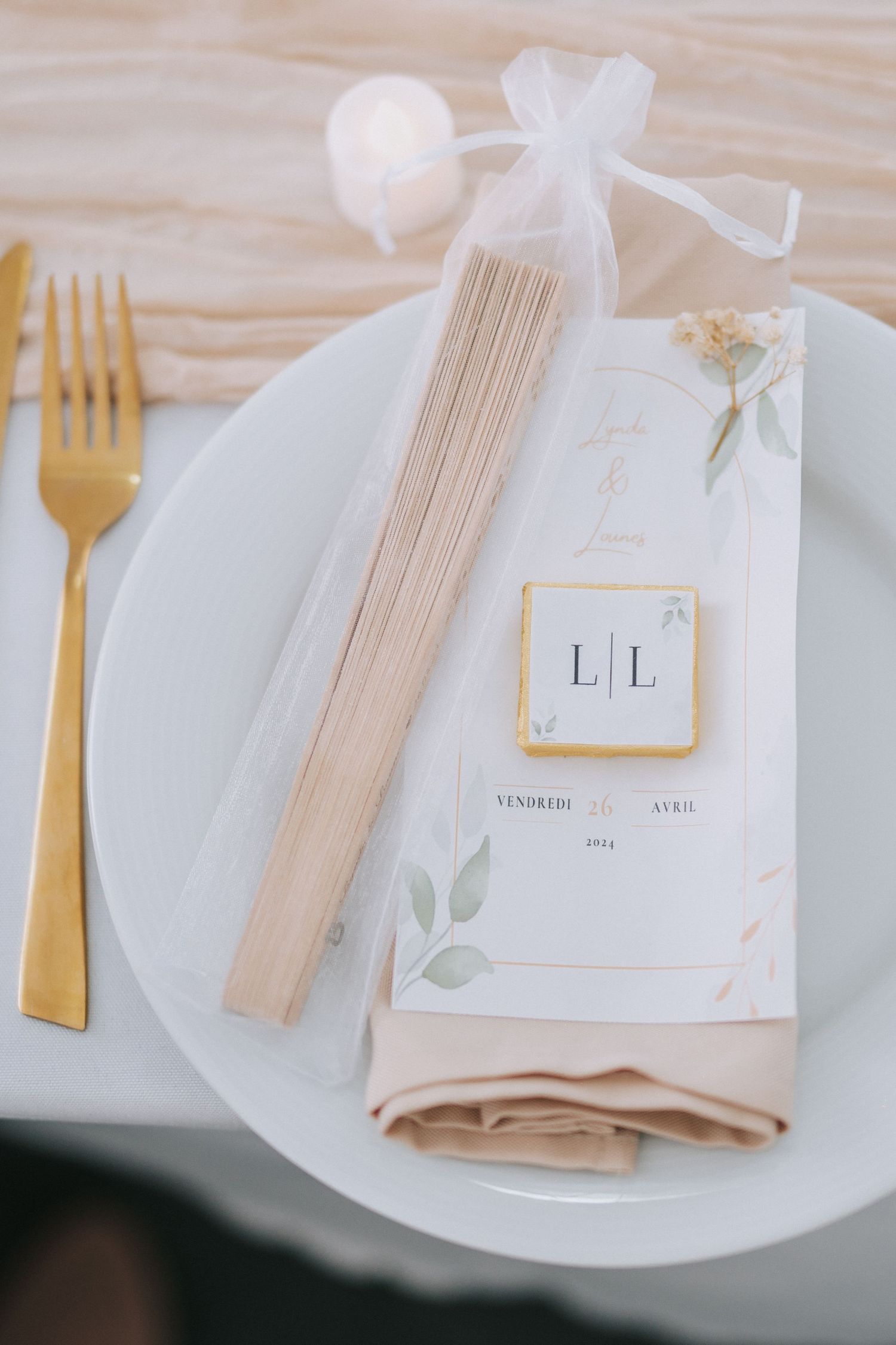 Place setting with gold cutlery, white plate, and romantic wedding favor in organza bag.