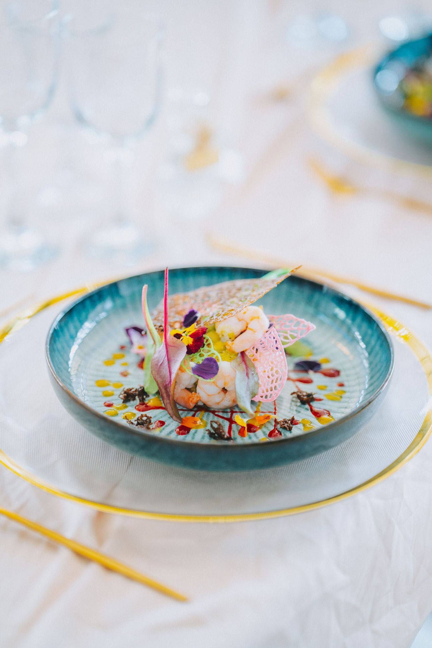 Elegant plated dessert with pink meringue and edible flowers on a turquoise ceramic plate with gold accents.