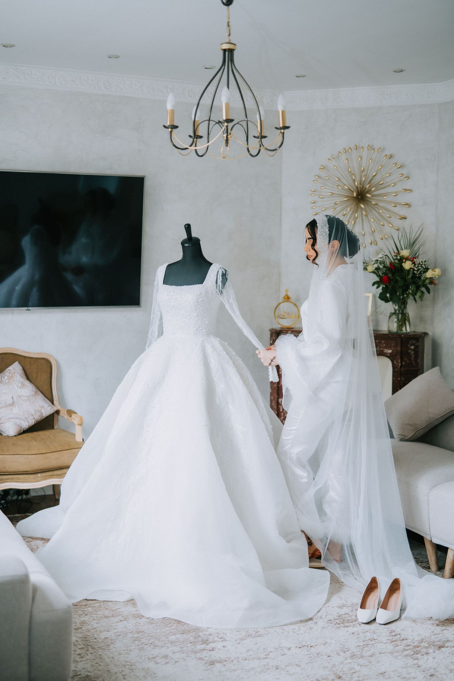Two elegant white wedding dresses on display in a room with a vintage chandelier and decorative wall art.