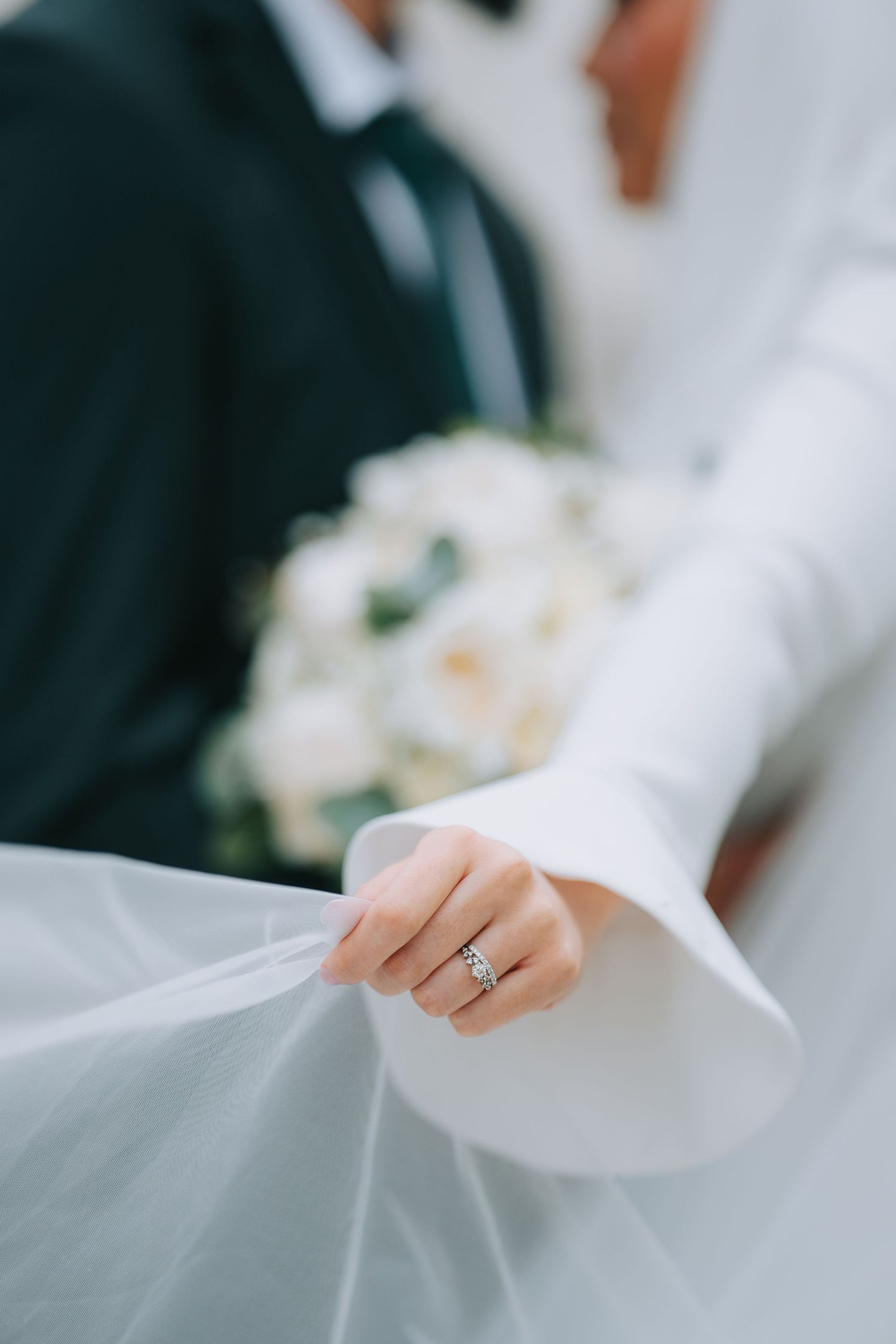 A close-up shot of a sparkling engagement ring on a bride's finger holding delicate white tulle veil.