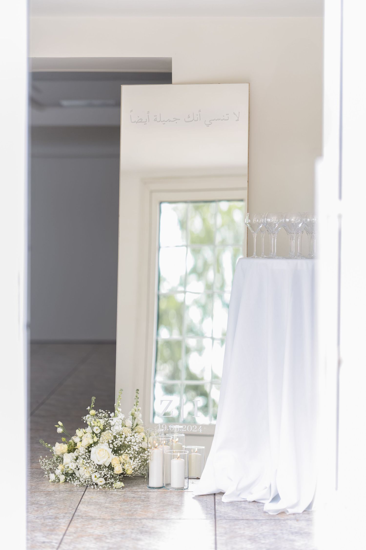 White wedding dress and floral bouquet displayed next to a full-length mirror in a bright, airy room.