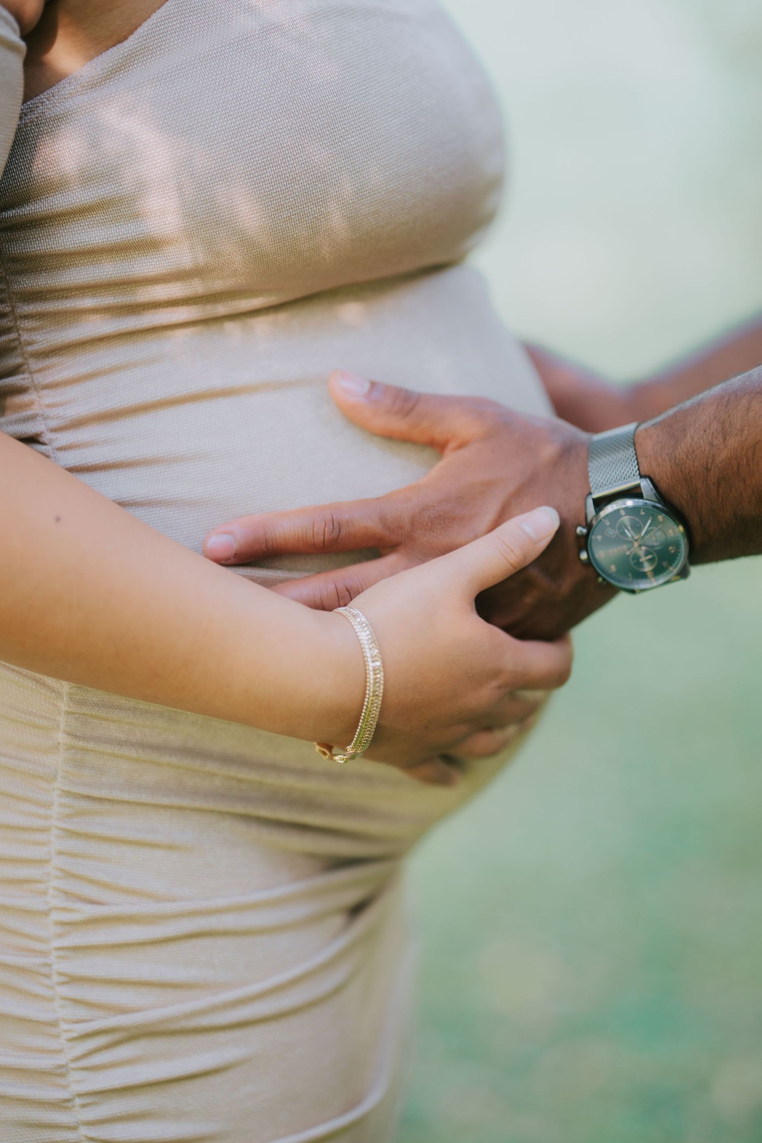 Close up of a pregnant woman's belly with hands tenderly touching her maternity dress in soft natural light.