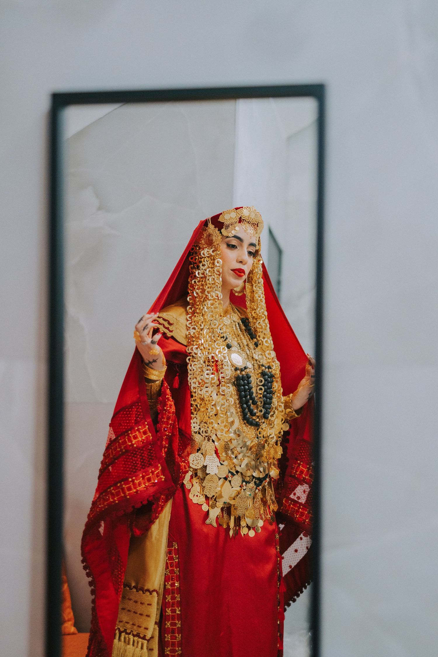 Traditional bridal attire with red dupatta and ornate gold jewelry reflected in mirror.