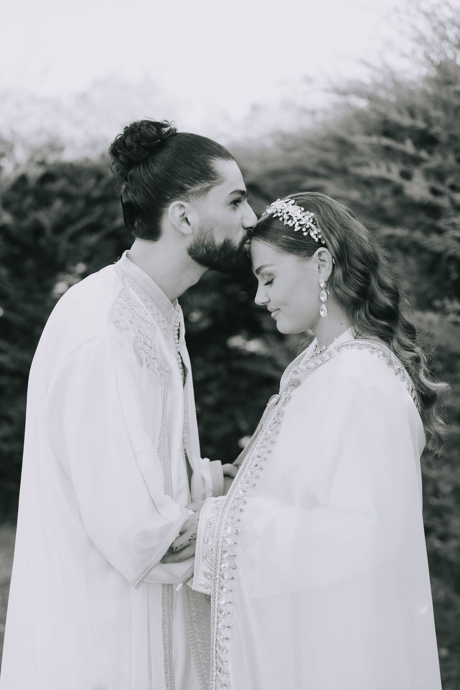 Romantic couple in traditional white wedding attire sharing an intimate moment outdoors.