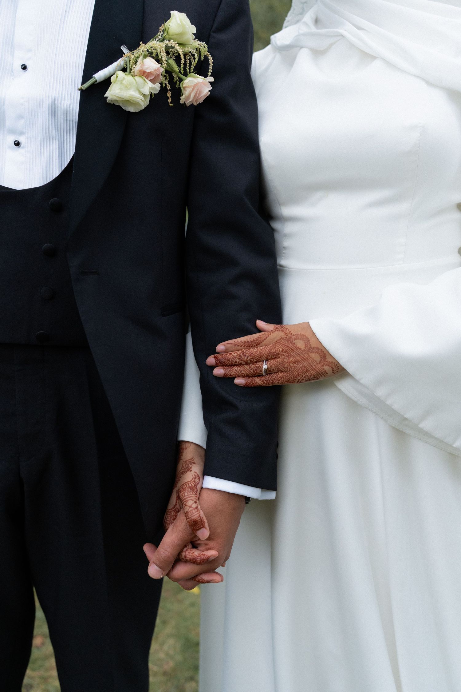 A close-up view of newlyweds holding hands, showing the bride in white and groom in black formal attire.