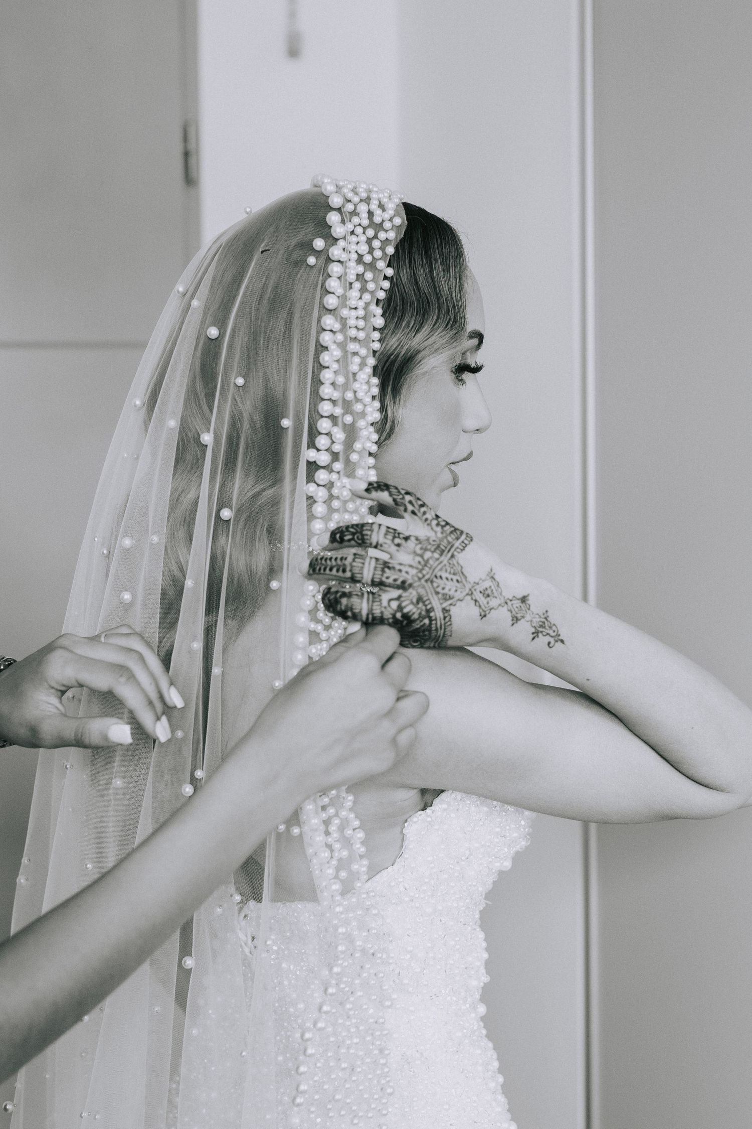 A black and white portrait of a bride wearing a beaded veil and traditional Indian bridal jewelry.