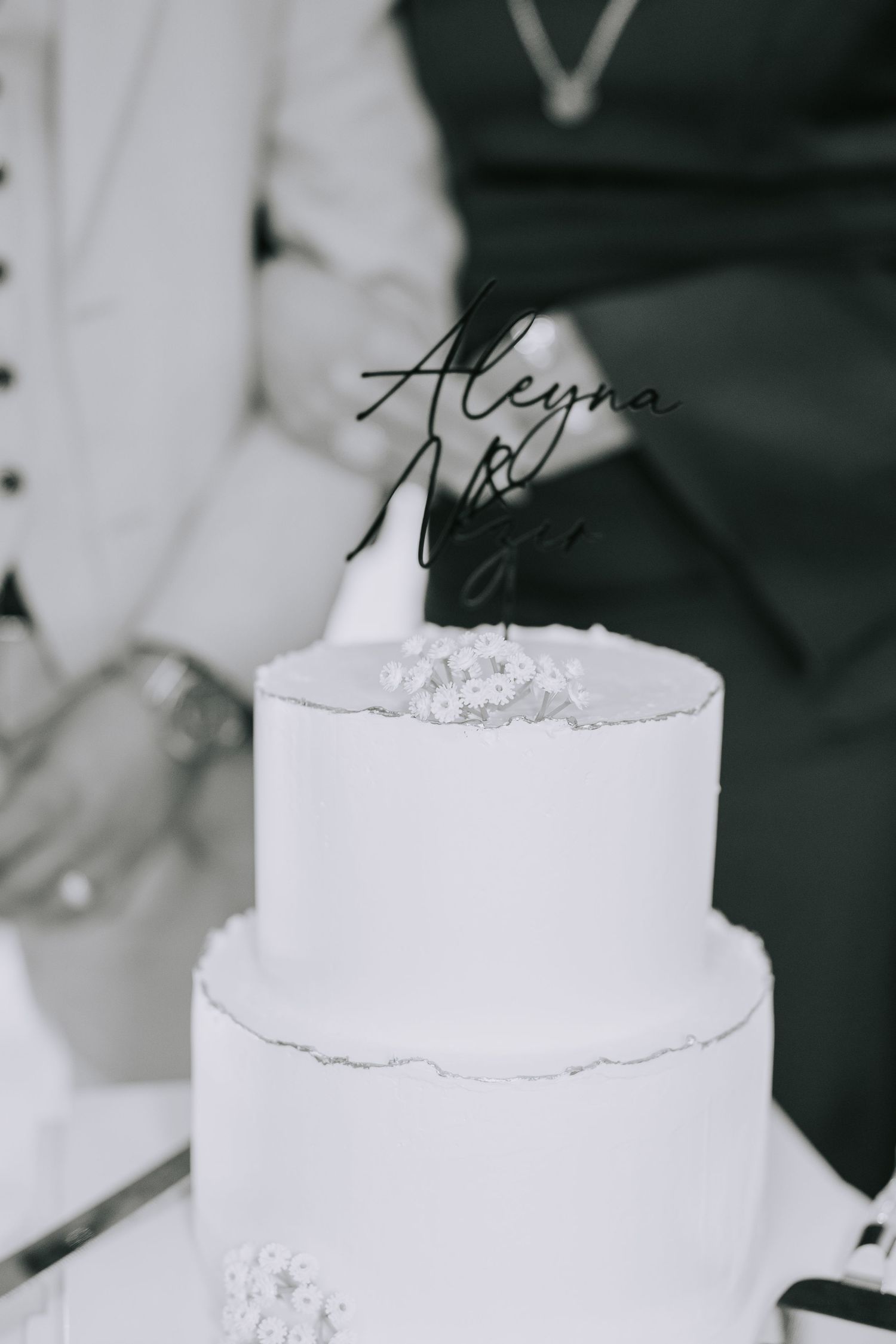 White two-tier wedding cake with a black calligraphy name topper.
