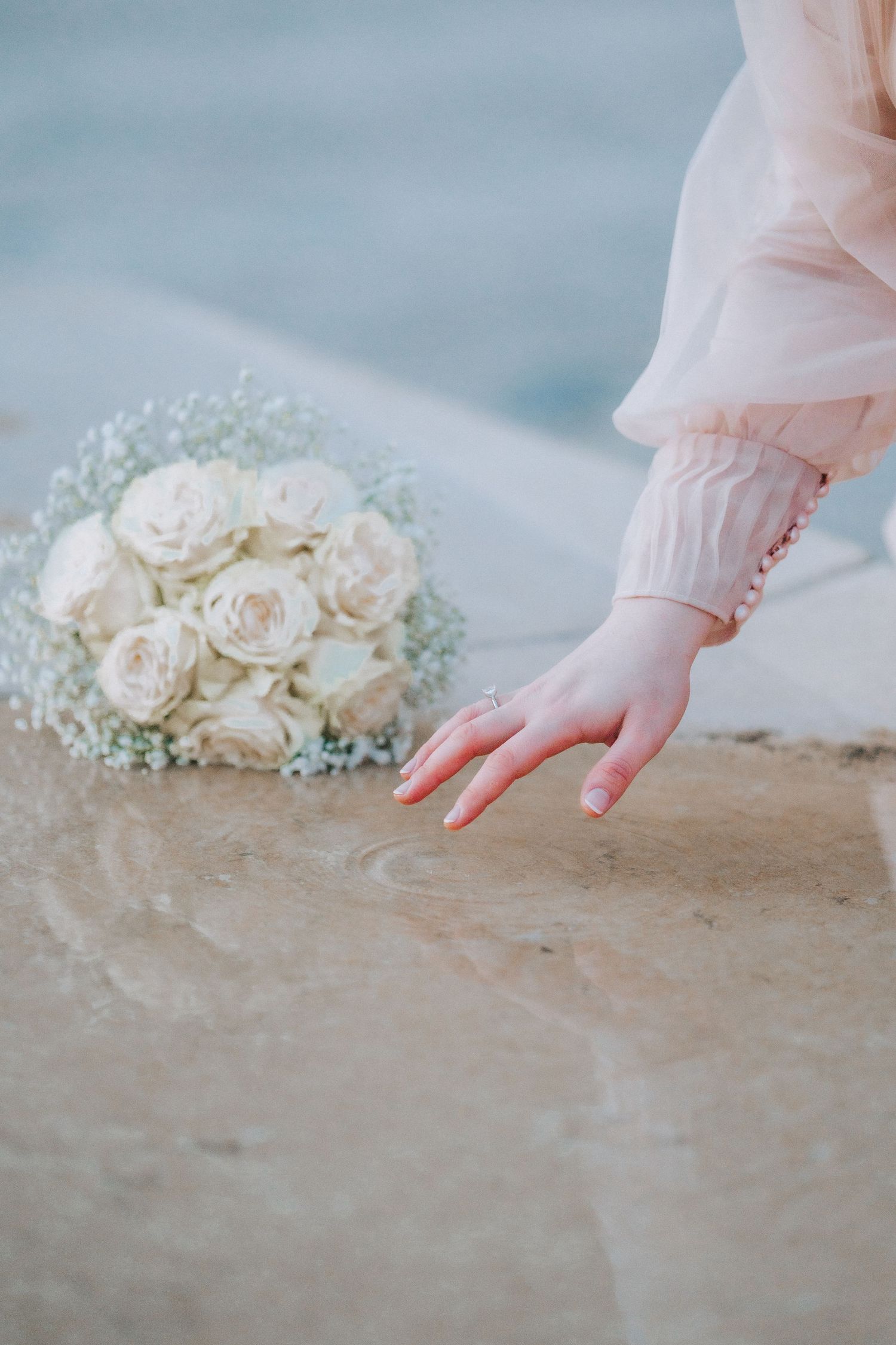 White rose bouquet with baby's breath beside a delicate hand with pink nails.