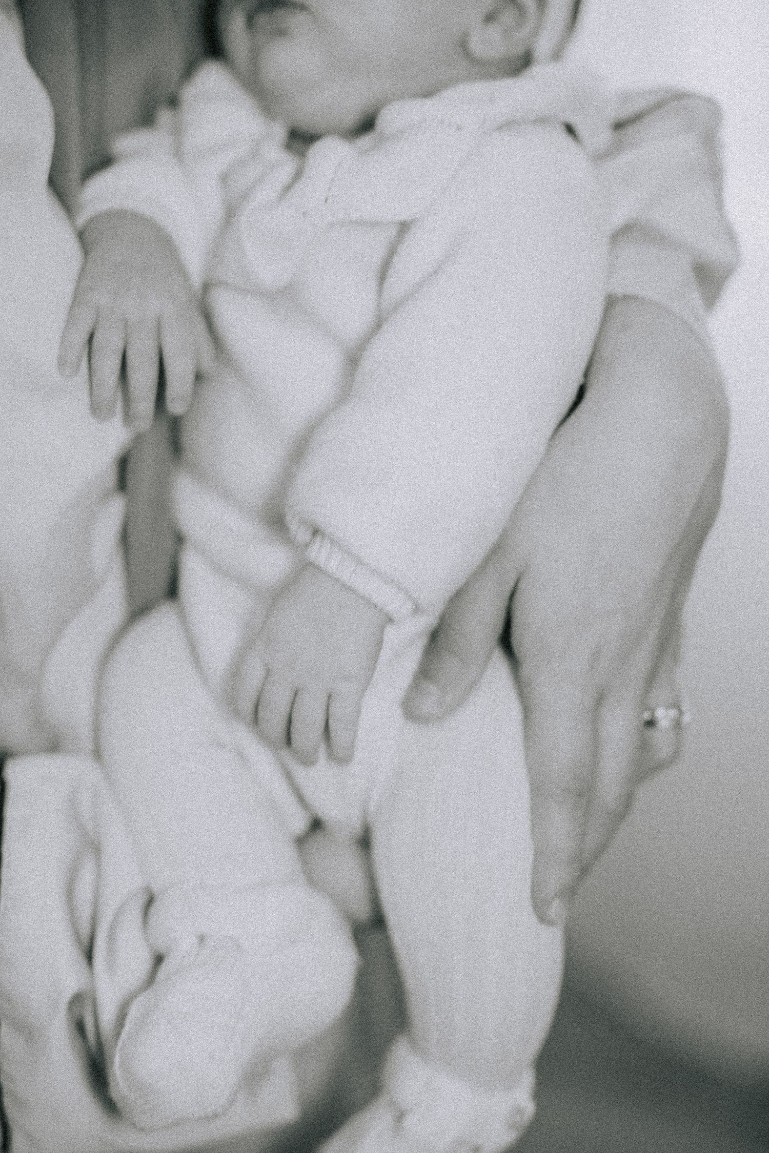 Black and white close-up of sleeping baby wearing white onesie.