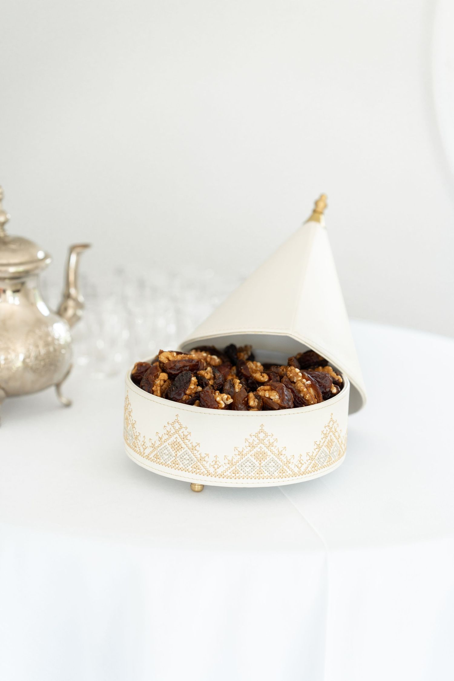 Moroccan tagine dish filled with nuts and dried fruits on a white tablecloth.