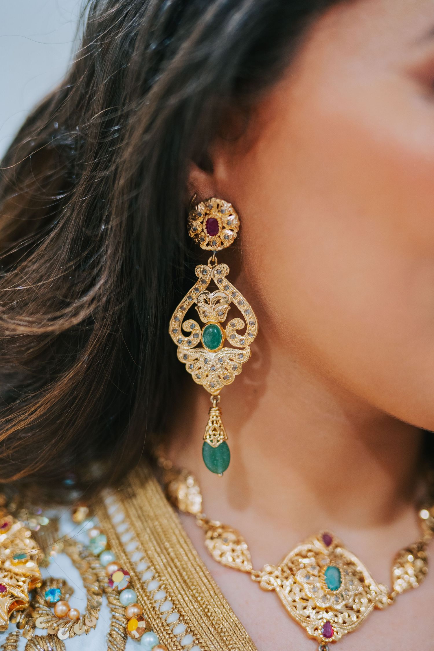 Ornate gold and turquoise chandelier earring with gemstones shown with matching necklace against blurred background.