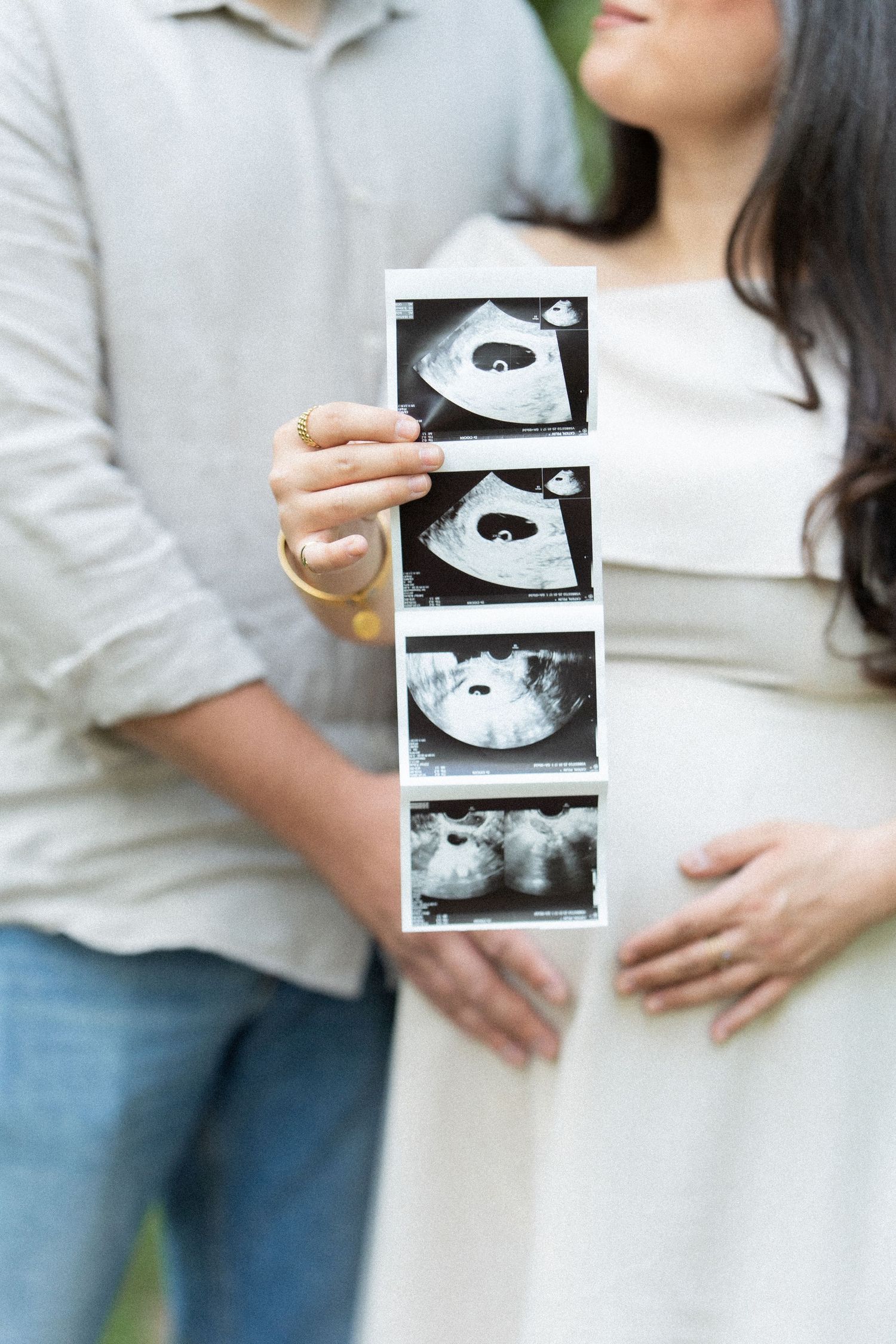 A couple holds ultrasound images while embracing in a tender pregnancy announcement moment.
