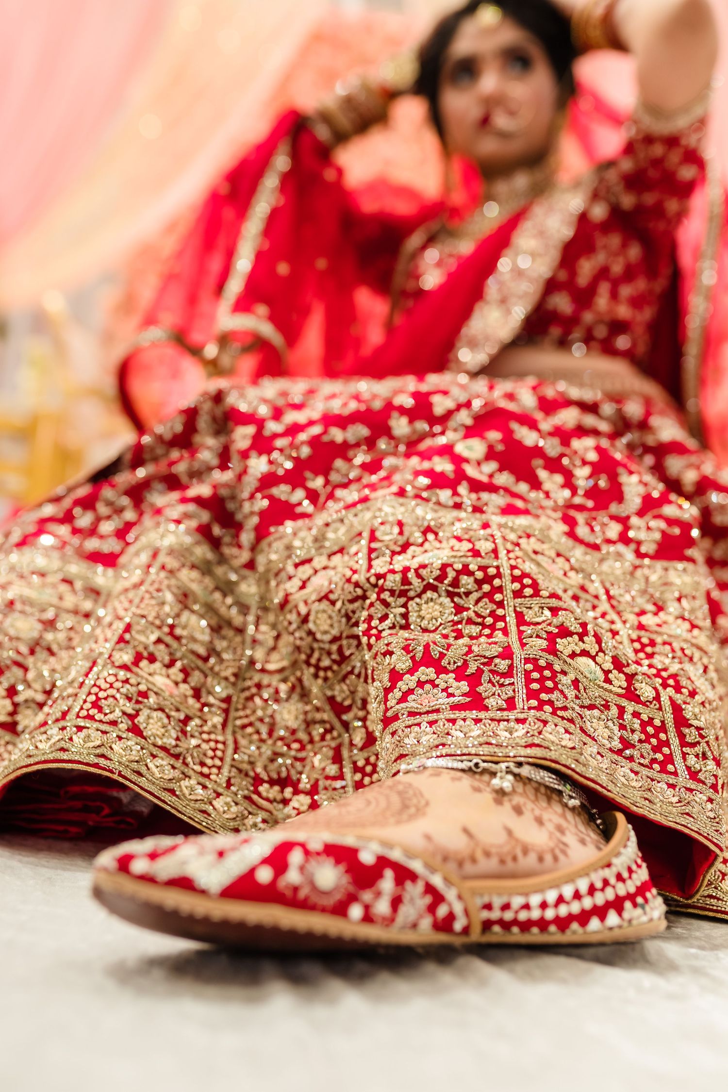 Close-up detail of an ornate red and gold Indian bridal lehenga with matching shoes.