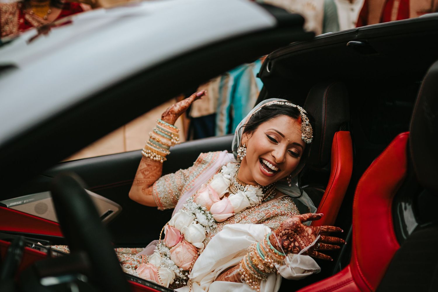 A person in traditional wedding attire smiles while sitting in a car with embellished jewelry and clothing.