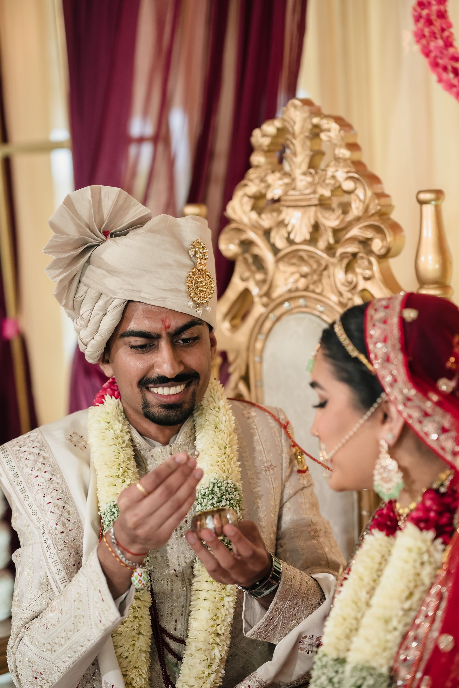 A traditional South Asian wedding ceremony showing couple in ornate cream and red attire with floral garlands.