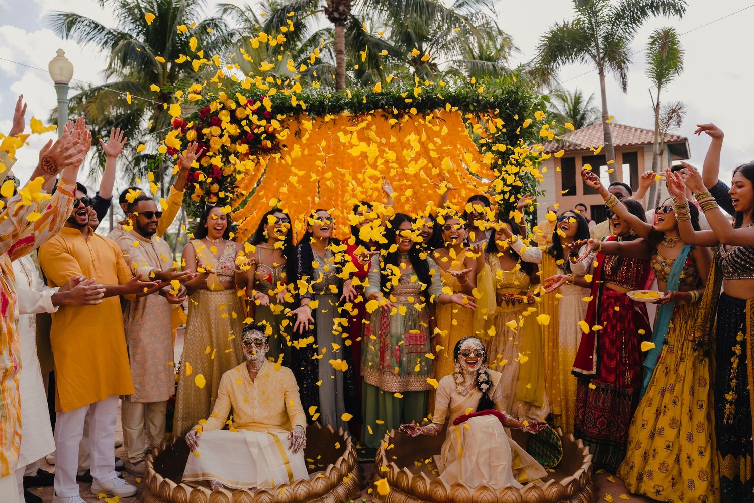 Traditional Indian wedding ceremony with yellow floral arch and guests in vibrant attire celebrating outdoors.