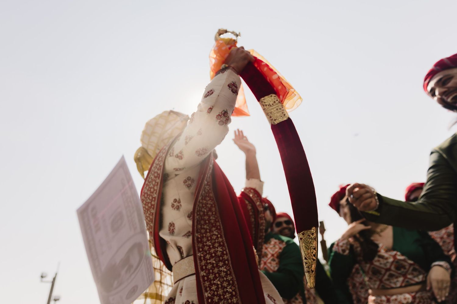 Traditional wedding ceremony moment captured with raised arms holding ceremonial cloth against sky.