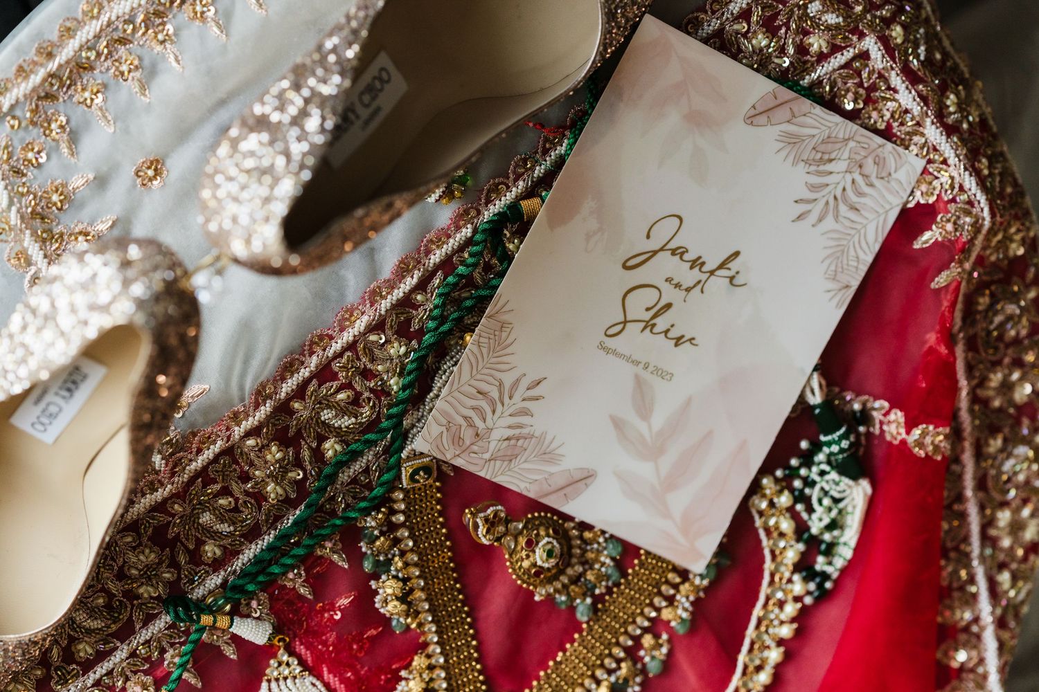 Wedding details featuring a white invitation with script text alongside red and gold traditional fabrics and accessories.