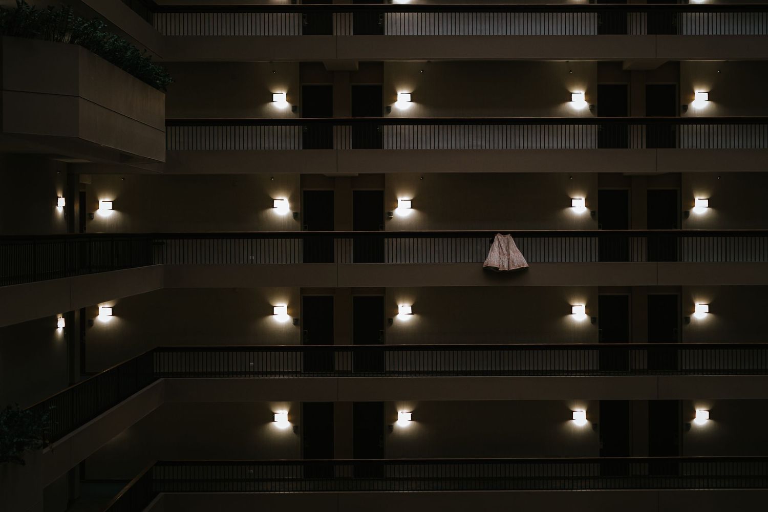 A white dress hangs illuminated among rows of lit wall sconces in a dark hotel atrium.