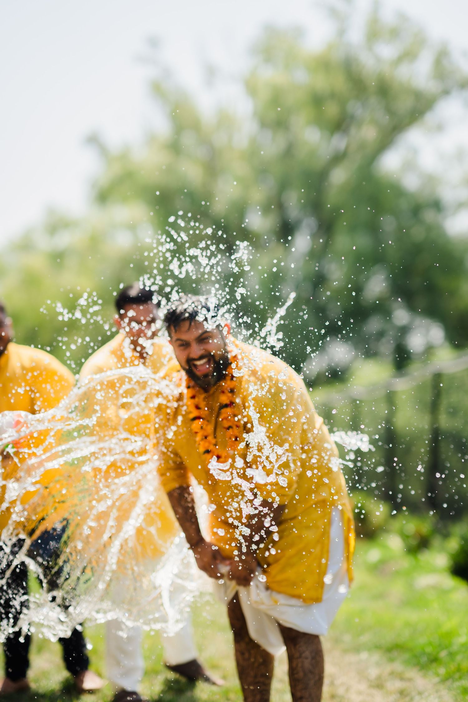 Water splashing on a couple wearing yellow outfits during a joyful outdoor celebration.