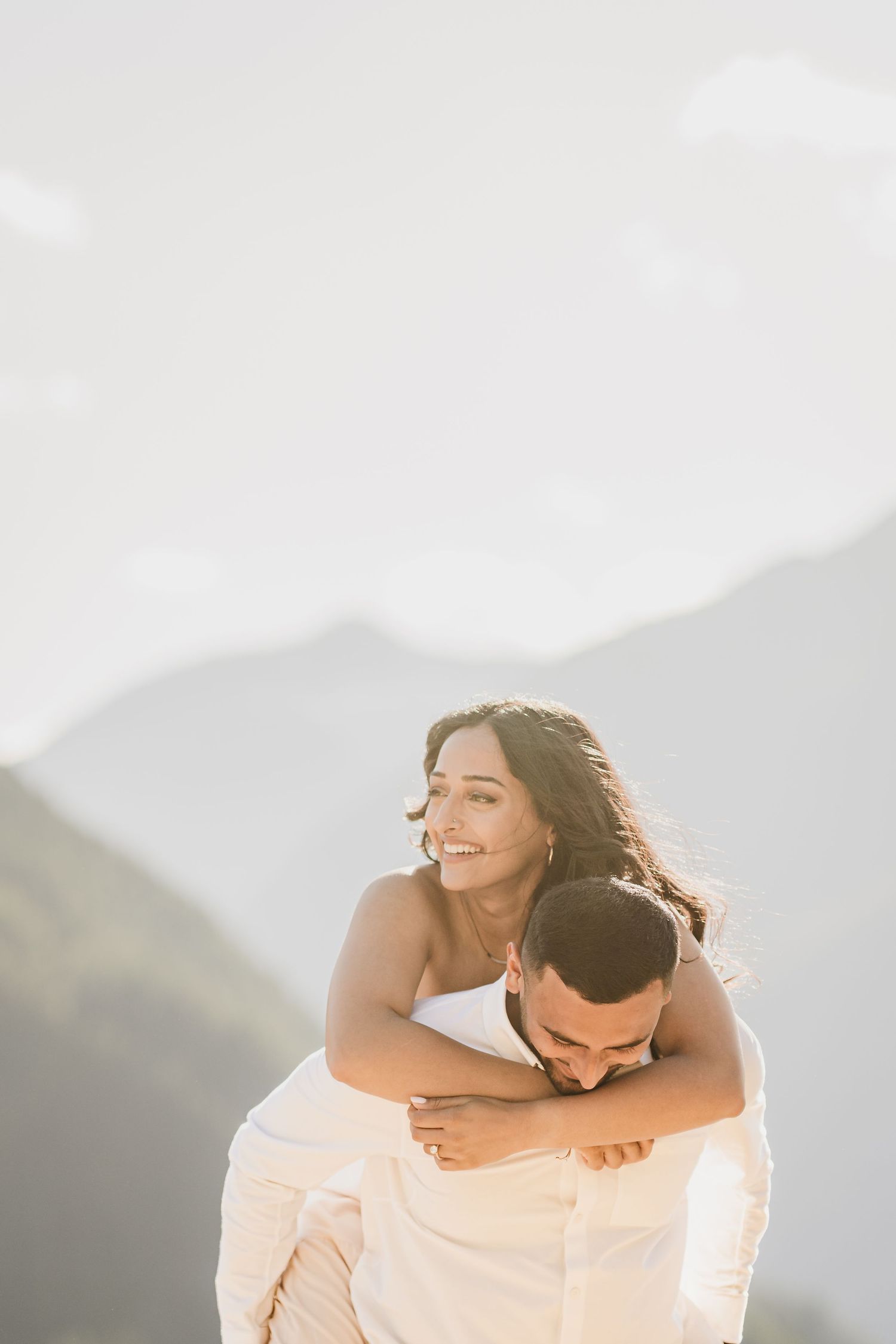 A joyful couple embraces against a mountainous backdrop at sunset.
