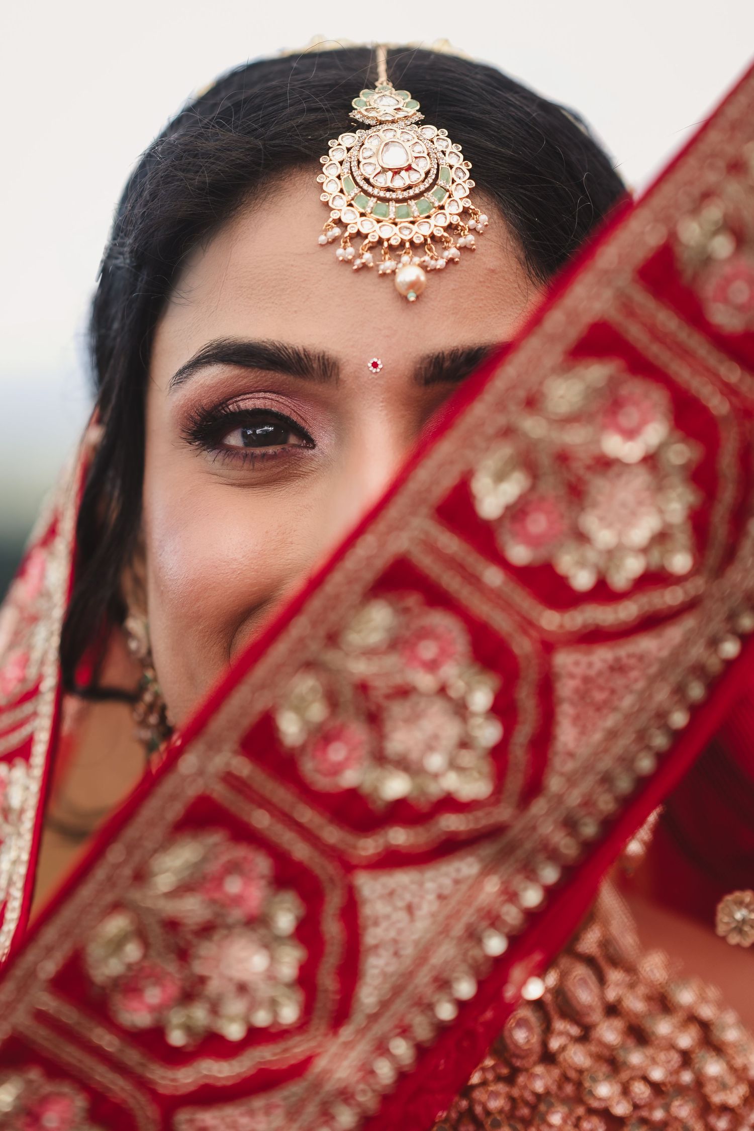 Indian bridal portrait showing intricate gold tikka jewelry and embroidered red dupatta.
