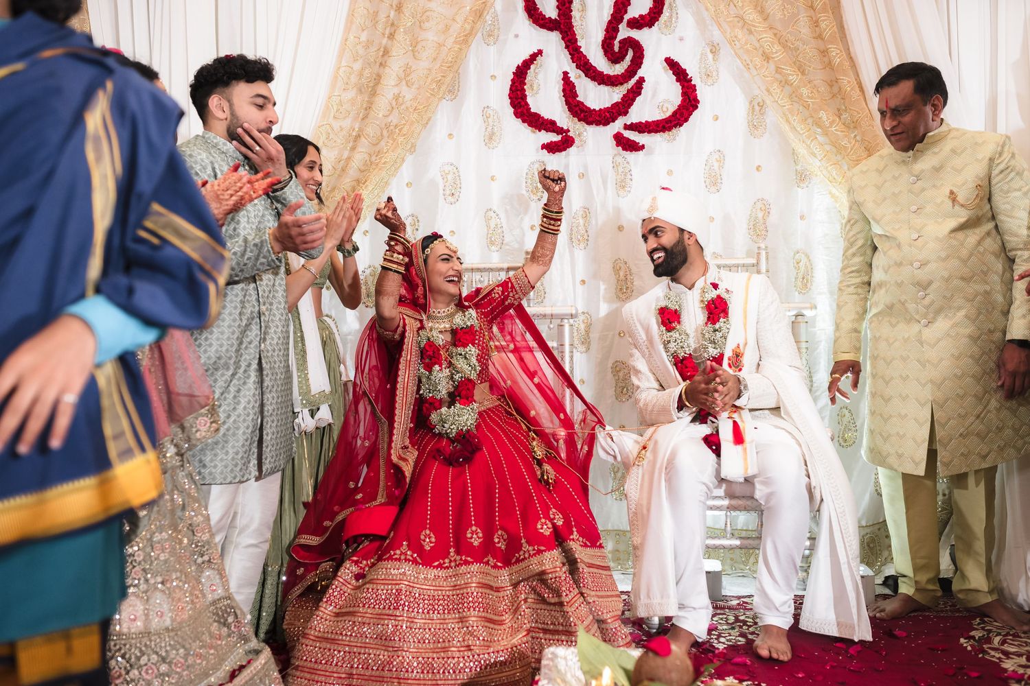 A traditional Indian wedding ceremony with the couple in red and white attire surrounded by family under decorative mandap.