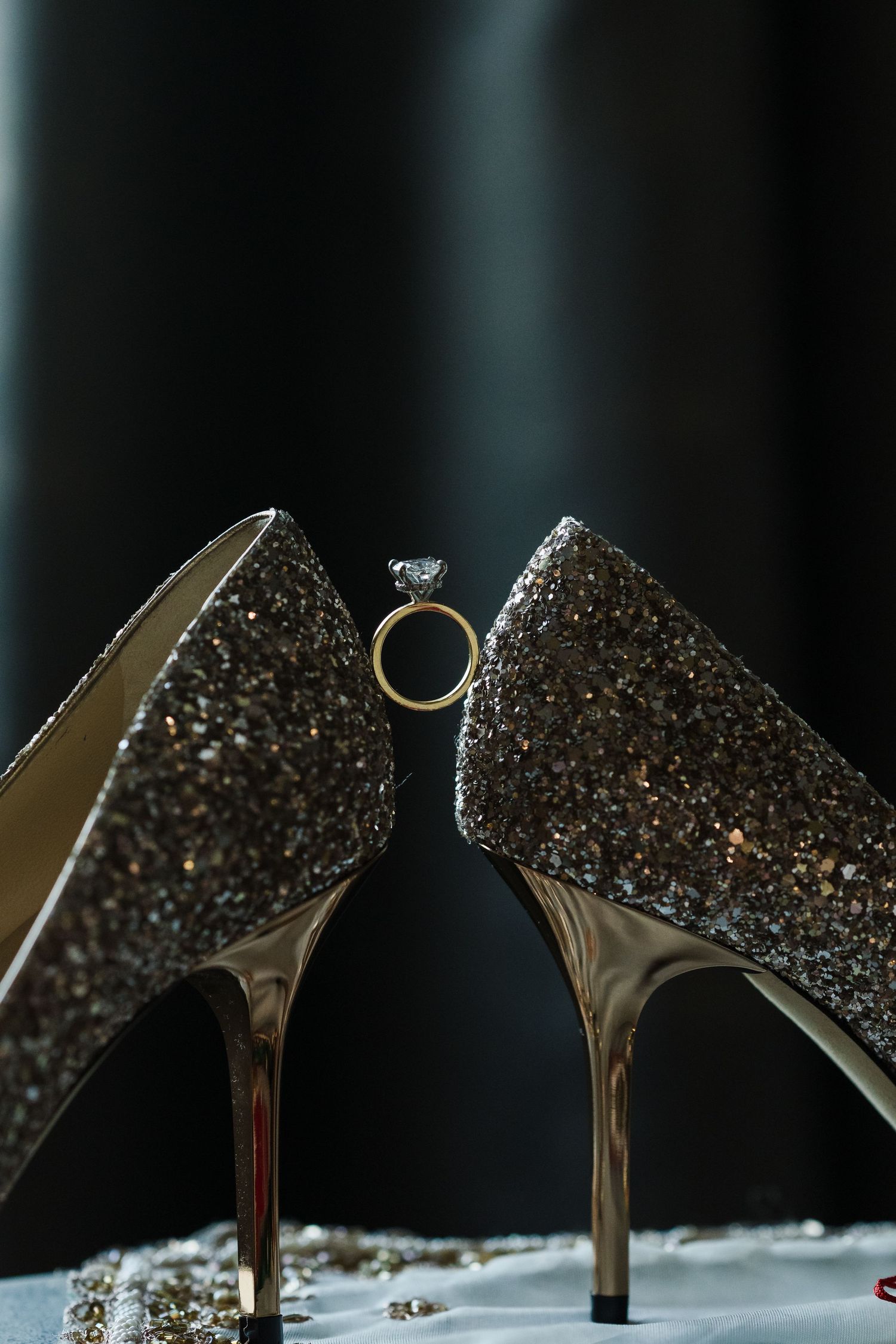 Elegant glittery wedding heels with diamond ring positioned between them.