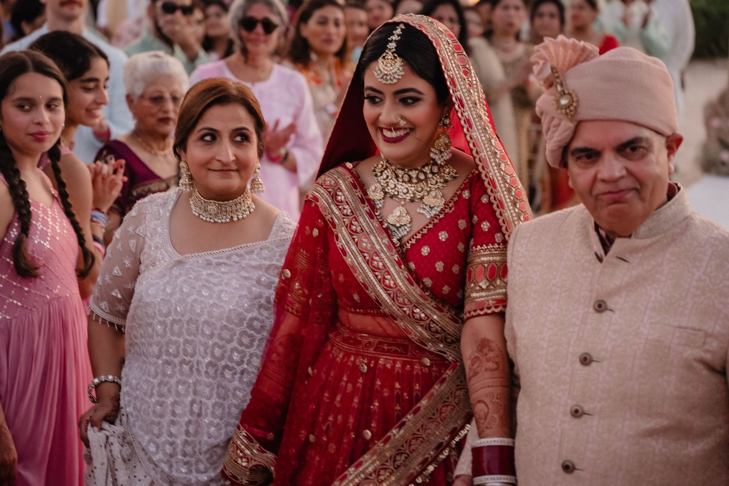 A traditional Indian wedding scene with wedding guests and a bride wearing an ornate red lehenga and jewelry.
