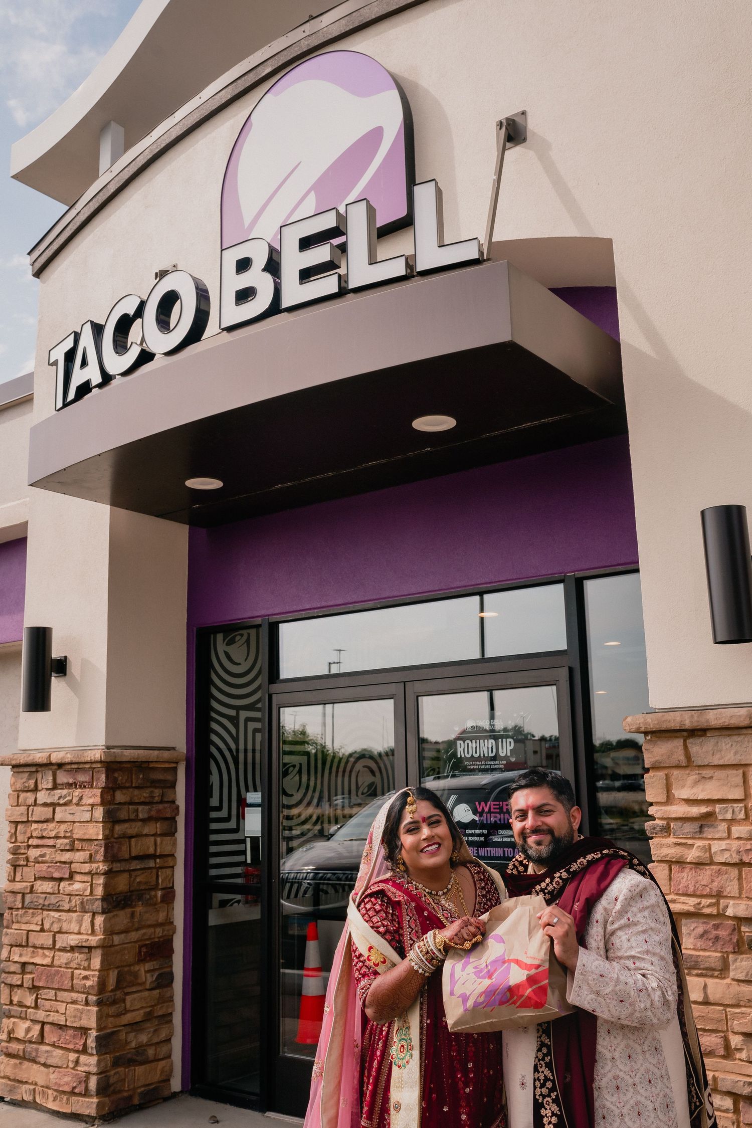 Wedding couple in traditional Indian attire posing outside Taco Bell restaurant.