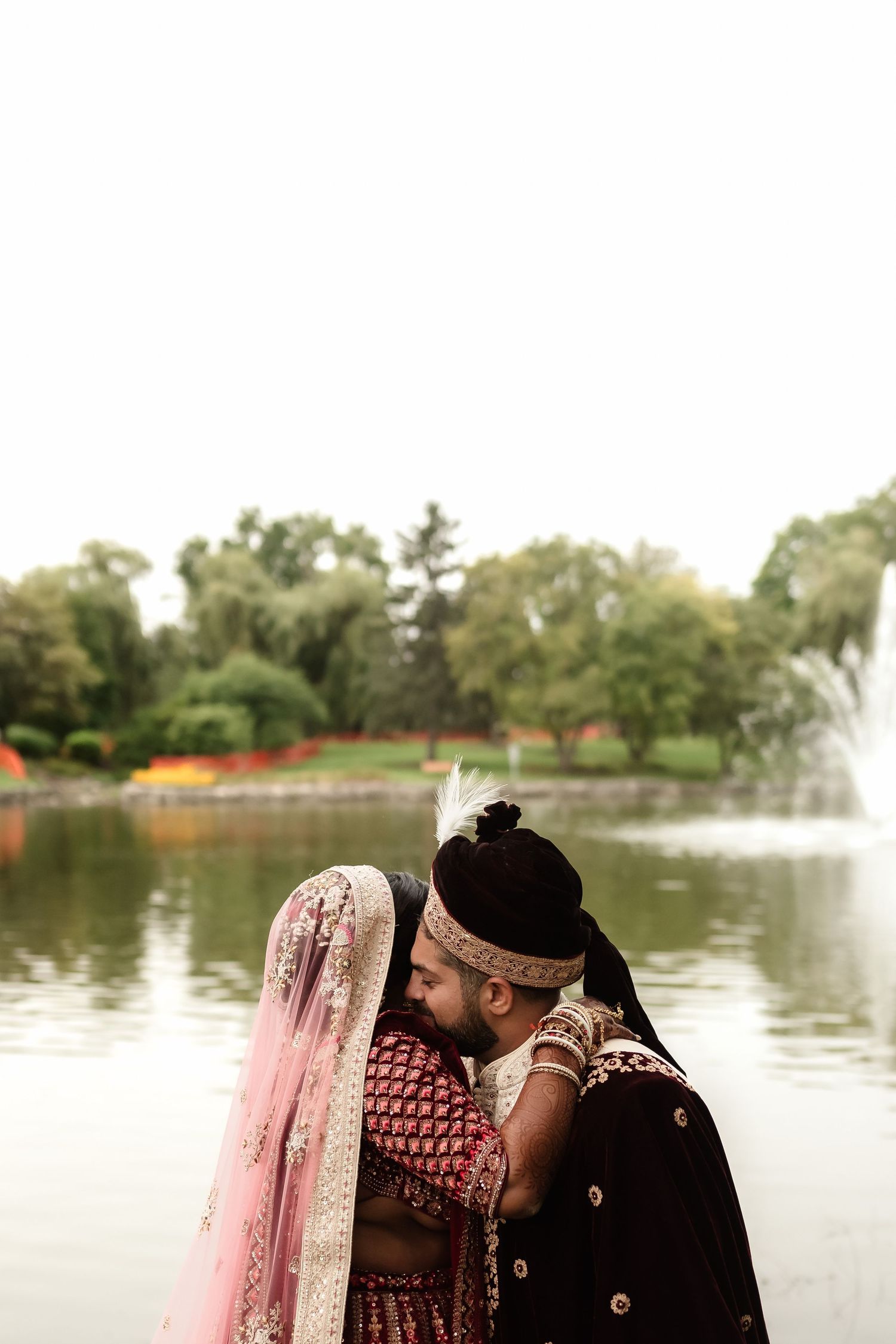 Romantic moment by a fountain with couple in traditional South Asian wedding attire.